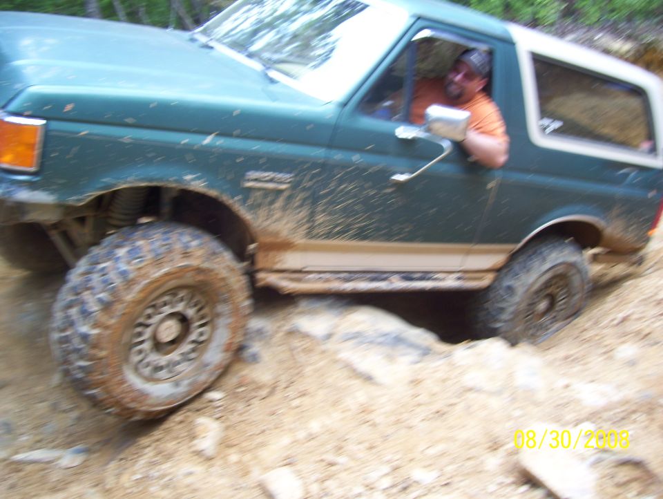 Green Ford Bronco with a man driving, going over rocks on a dirt trail