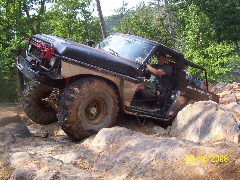 Black 1978 Ford Bronco off-roading over rocks, driver visible, modified exterior