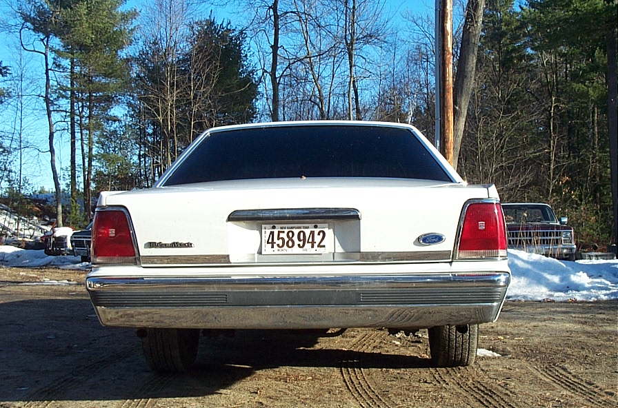 Rear view of white Ford LTD Crown Victoria sedan with NH plate 458942 on dirt lot