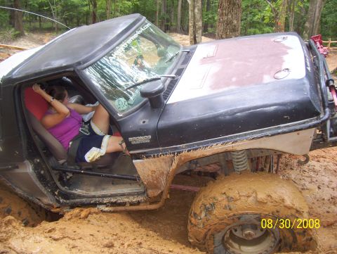1978 Ford Bronco - A woman sits in a mud-splattered 1978 Ford Bronco that is stuck in the dirt.