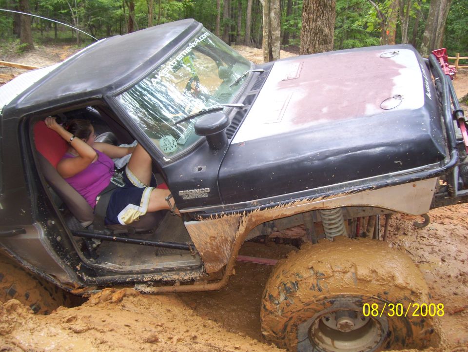 Mud-covered 1978 Ford Bronco with a woman inside, stuck in dirt