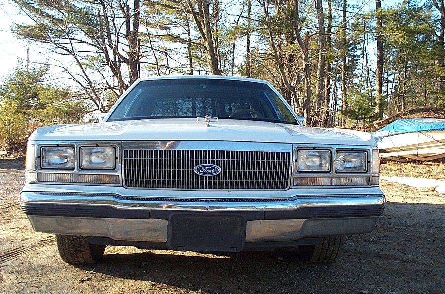 Front view of white Ford Crown Victoria showing grille, Ford oval and quad headlights