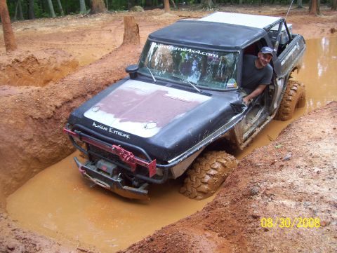 1978 Ford Bronco - A man is driving a heavily modified off-road vehicle through a muddy pit.