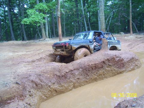 1978 Ford Bronco - This modified truck navigates a challenging muddy terrain with trees in the background.