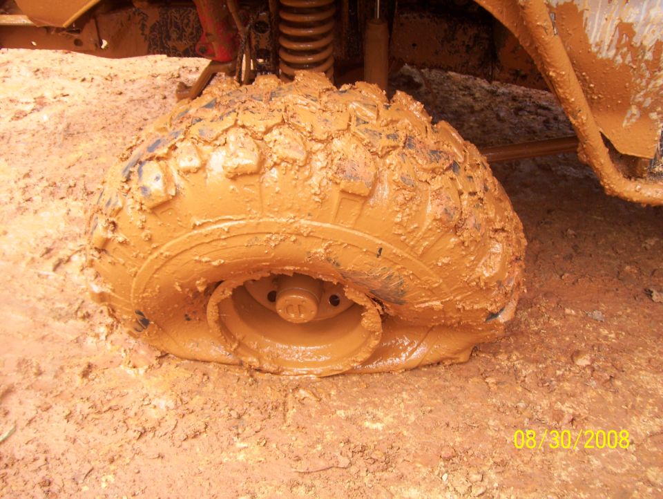 Mud-covered tire stuck in mud, showing suspension components and part of the vehicle body