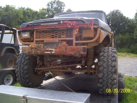 1978 Ford Bronco - A heavily modified truck, covered in mud, is secured to a trailer with chains.