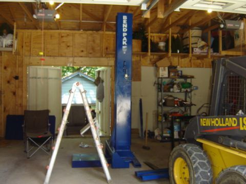 1992 Ford Bronco - A New Holland skid steer loader is parked in a garage next to a car lift.