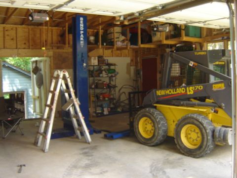 1992 Ford Bronco - A New Holland LS170 skid steer loader is parked inside a garage with a car lift.