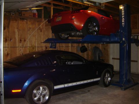 1992 Ford Bronco - A blue Mustang and a red sports car are parked on a car lift inside a garage.