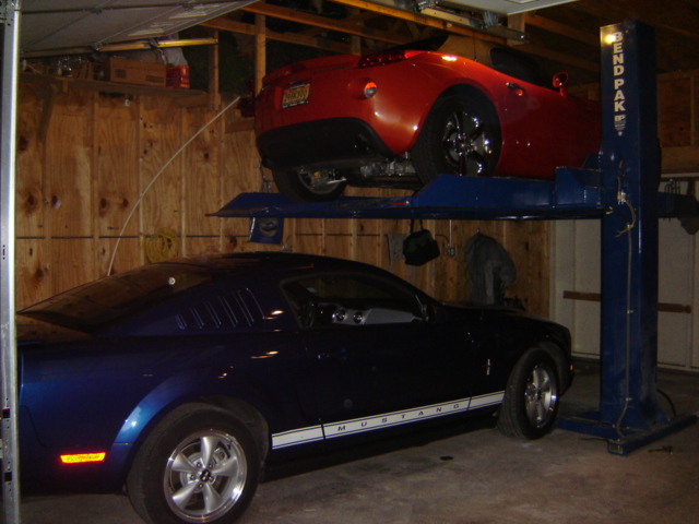 Blue Mustang and red sports car on a two-post lift in a garage