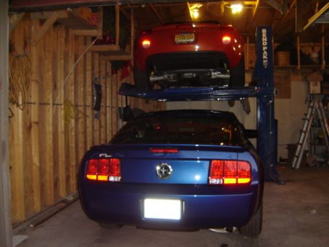 1992 Ford Bronco - Two cars, a blue Ford Mustang and a red car, are parked on a two-post car lift inside a garage.