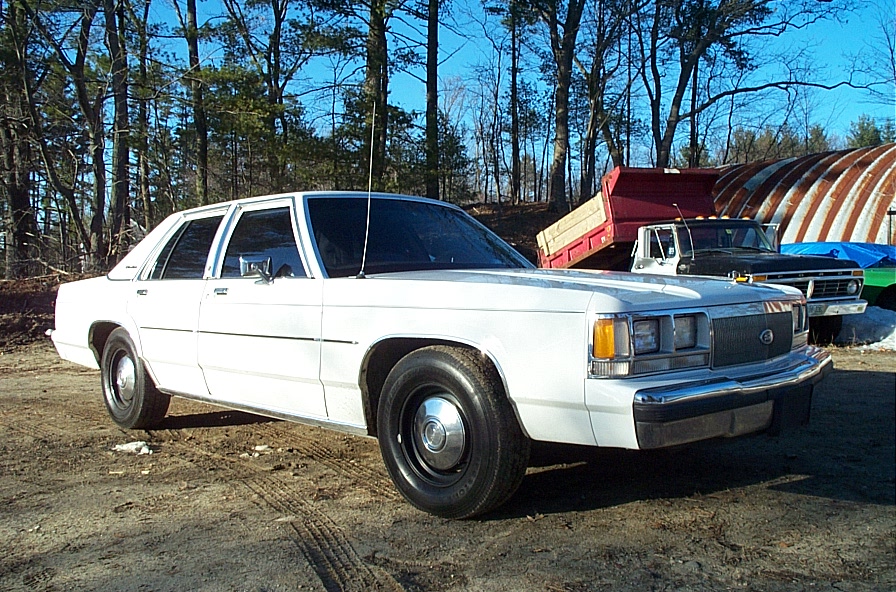 White Ford LTD Crown Victoria sedan with black steel wheels parked on a dirt lot