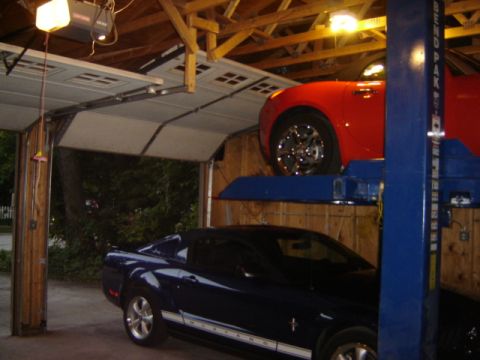1992 Ford Bronco - Two Ford Mustangs are parked in a garage, one is on a car lift and the other is on top of it.