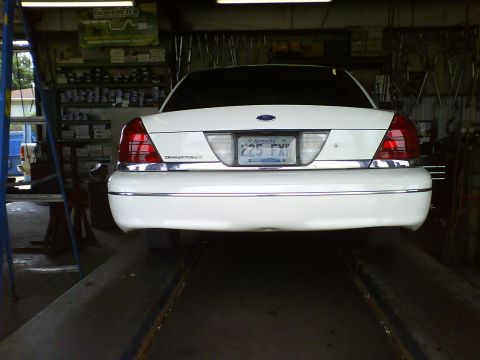 2003 Ford Crown Victoria - Rear view of a white 2003 Ford Crown Victoria on a car lift inside a repair shop.