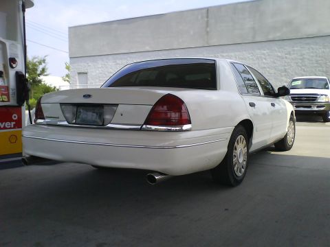 2003 Ford Crown Victoria - Rear view of a white 2003 Ford Crown Victoria parked at a gas station with another vehicle visible in the background.