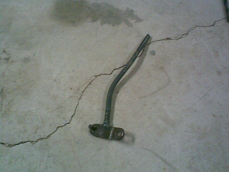 Bare bent steel shift lever with bolt-on base lying on a concrete floor