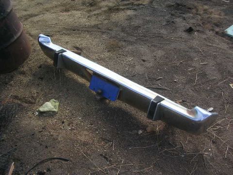 1975 Ford Ranchero - A detached chrome bumper with black accents rests on the ground next to a large metal object.