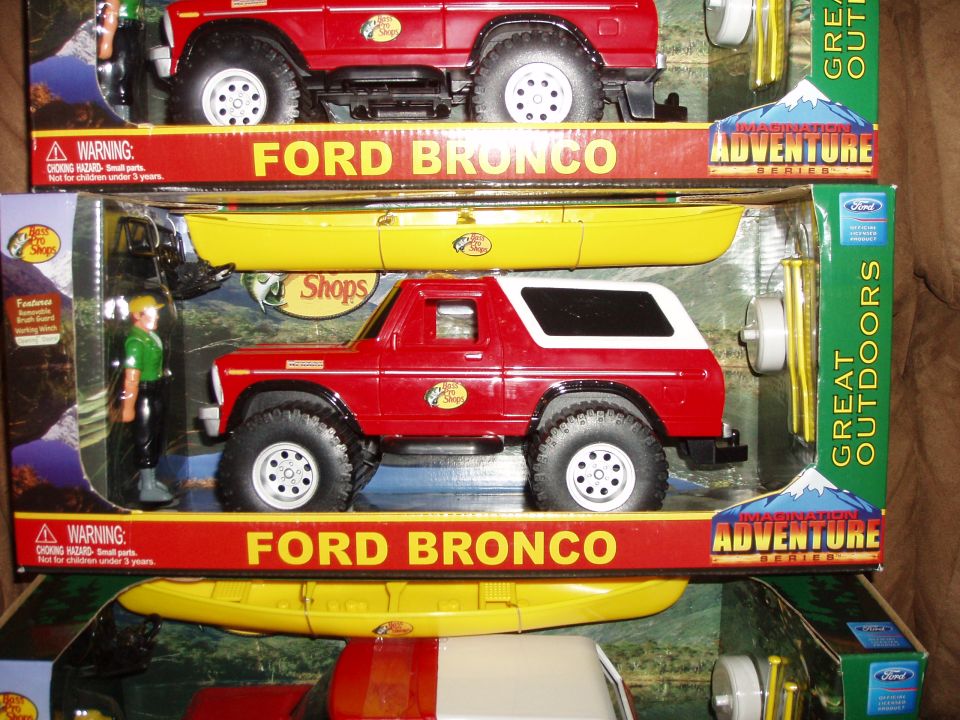 Two toy Ford Broncos in packaging, one with a yellow kayak accessory. The lower Bronco is red with a white top