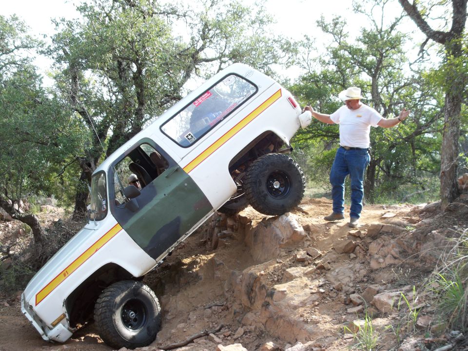 White and green SUV with yellow stripe, lifted suspension, and large tires, angled on a rocky incline