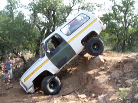 1996 Ford Bronco - This white SUV, camouflage door panels and a yellow stripe, navigates a challenging rocky incline off-road.