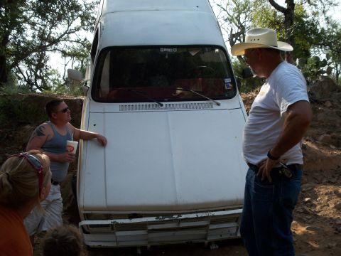 1996 Ford Bronco - People observe a white van stuck on a rough, dirt road in a wooded area.