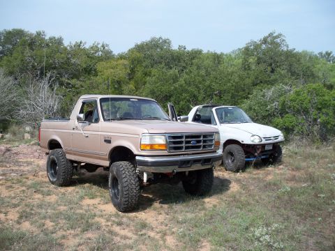 1996 Ford Bronco - Two modified off-road vehicles are parked outdoors in a natural setting.