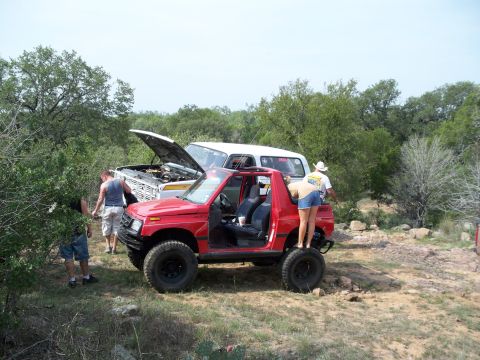 1996 Ford Bronco - Two SUVs are parked in a dry, wooded area with people gathered around them.