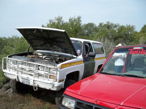 1996 Ford Bronco - A white and green SUV with its hood open is parked next to a red vehicle in an outdoor setting.