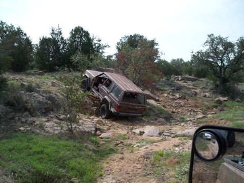1996 Ford Bronco - A Jeep Cherokee XJ navigates a challenging rocky incline on a sunny day.
