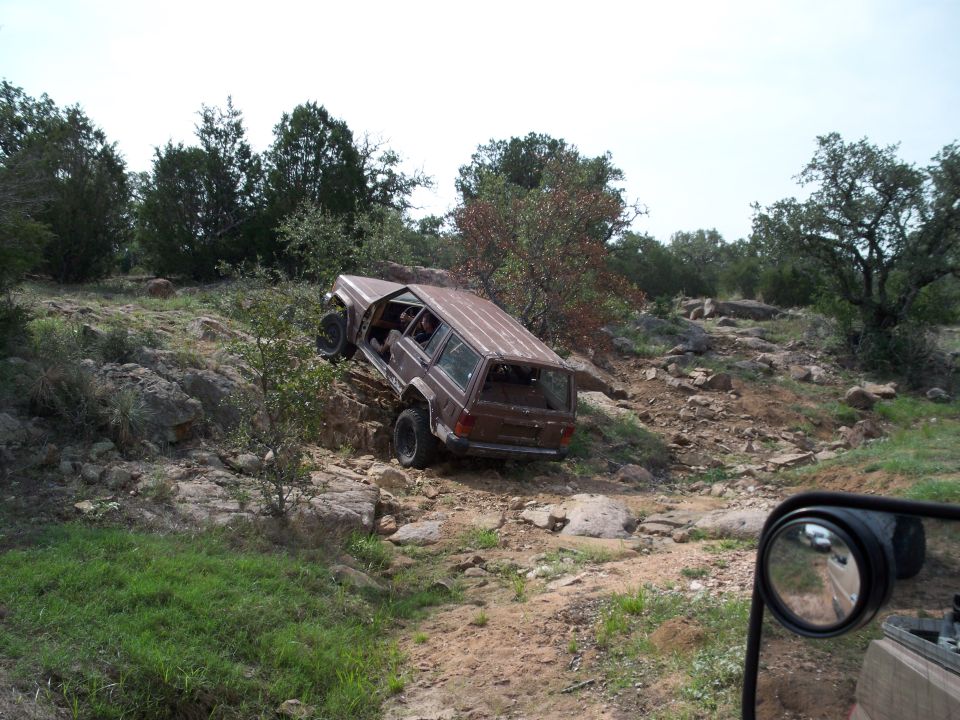 Brown Jeep Cherokee XJ climbing rocky hill. Taken from another vehicle's side mirror