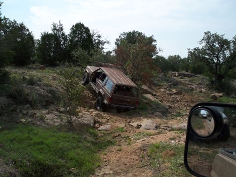 1996 Ford Bronco - A brown Jeep Cherokee XJ navigates a rocky trail, its driver's side door ajar, as seen from another vehicle.