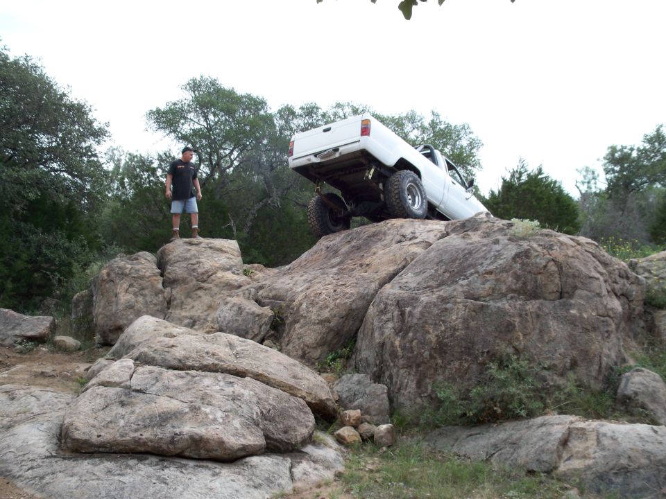 White pickup truck with lifted suspension climbing large rocks