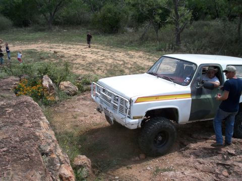 1996 Ford Bronco - Off-road SUV with custom paint and brush guard navigates rocky terrain.