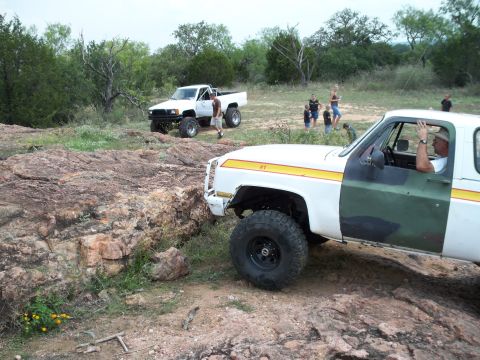 1996 Ford Bronco - Two trucks navigate a rocky, off-road terrain with spectators observing the action.