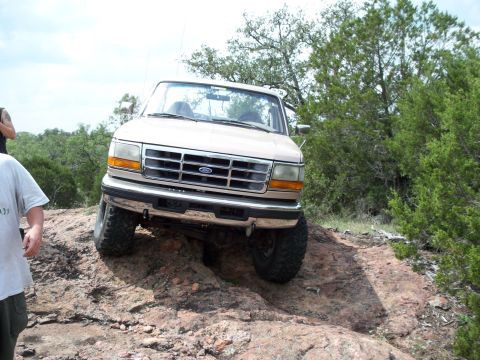 1996 Ford Bronco - A tan Ford Bronco navigates a challenging rocky trail with its front wheels angled.