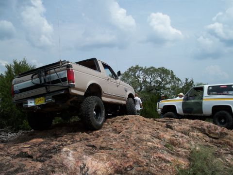 1996 Ford Bronco - Two off-road SUVs, a Ford Bronco and a Chevy K5 Blazer, navigate rocky terrain under a cloudy sky.