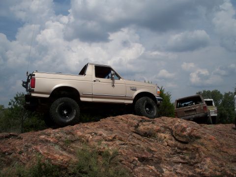 1996 Ford Bronco - A 1996 Ford Bronco navigates rocky terrain under a cloudy sky.