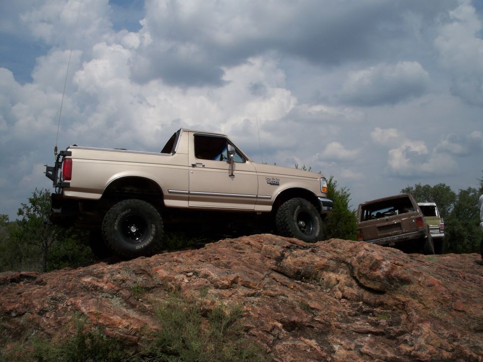 Tan 1996 Ford Bronco on rocks with another SUV behind it