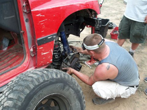 1996 Ford Bronco - A man works on the brake assembly of a red SUV with its front wheel removed.
