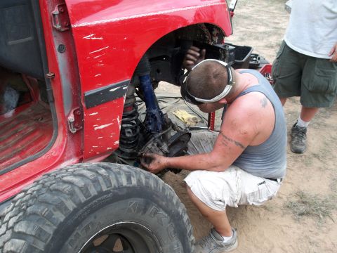 1996 Ford Bronco - A man works on the front suspension of a red SUV, with another person standing nearby.