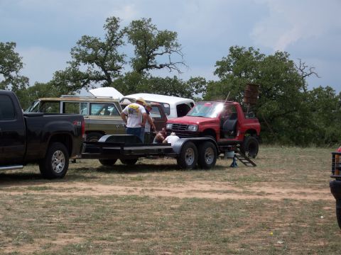 1996 Ford Bronco - Several vehicles are parked outdoors, including a red pickup truck on a trailer and a brown station wagon.