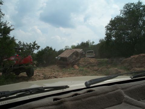 1996 Ford Bronco - Multiple off-road vehicles are seen on a challenging dirt path surrounded by vegetation.