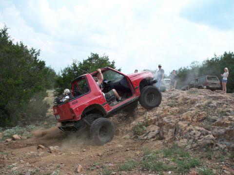 1996 Ford Bronco - A red off-road vehicle navigates a challenging rocky terrain with spectators watching.