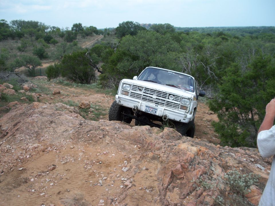 White off-road SUV with a prominent grille and aftermarket bumper, navigating rocky terrain