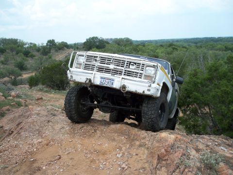 1996 Ford Bronco - This white off-road truck navigates a rocky incline, its brush guard prominent against the landscape.