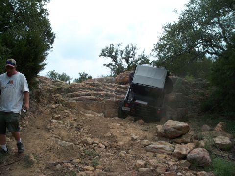 1996 Ford Bronco - Off-road vehicle attempting to climb a steep, rocky terrain with a person observing.