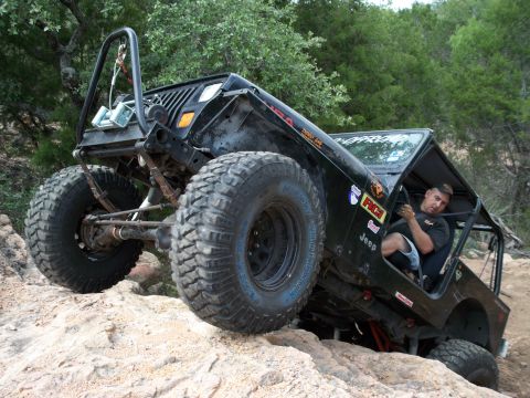 1996 Ford Bronco - A driver navigates a heavily modified Jeep Wrangler over a rocky trail.