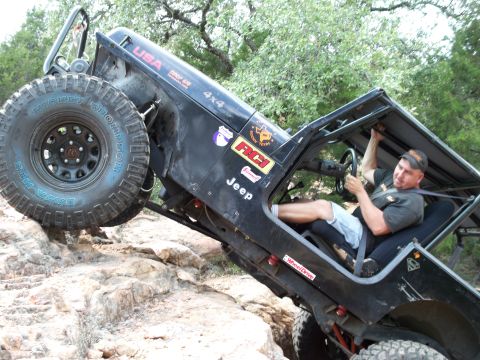 1996 Ford Bronco - A black Jeep Wrangler navigates a rocky trail with a driver inside.
