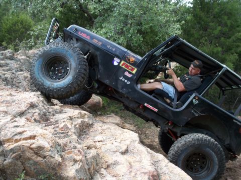 1996 Ford Bronco - A black Jeep Wrangler navigates a steep, rocky trail with its driver behind the wheel.