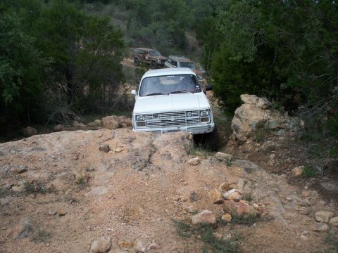 1996 Ford Bronco - White Chevrolet pickup truck drives over rough terrain, with other vehicles following.